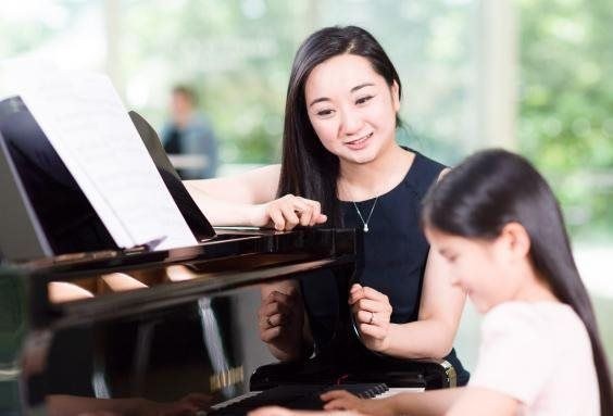 girl plays on piano and teacher listens to her